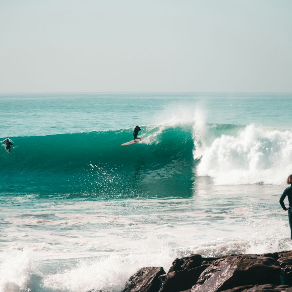 a person standing on a rock in front of a wave